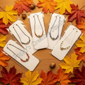 Handmade beaded evil eye bracelets on display cards surrounded by autumn fall leaves on rustic wooden surface