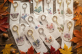 Handmade butterfly keychains surrounded by autumn maple leaves and acorns on rustic wooden surface